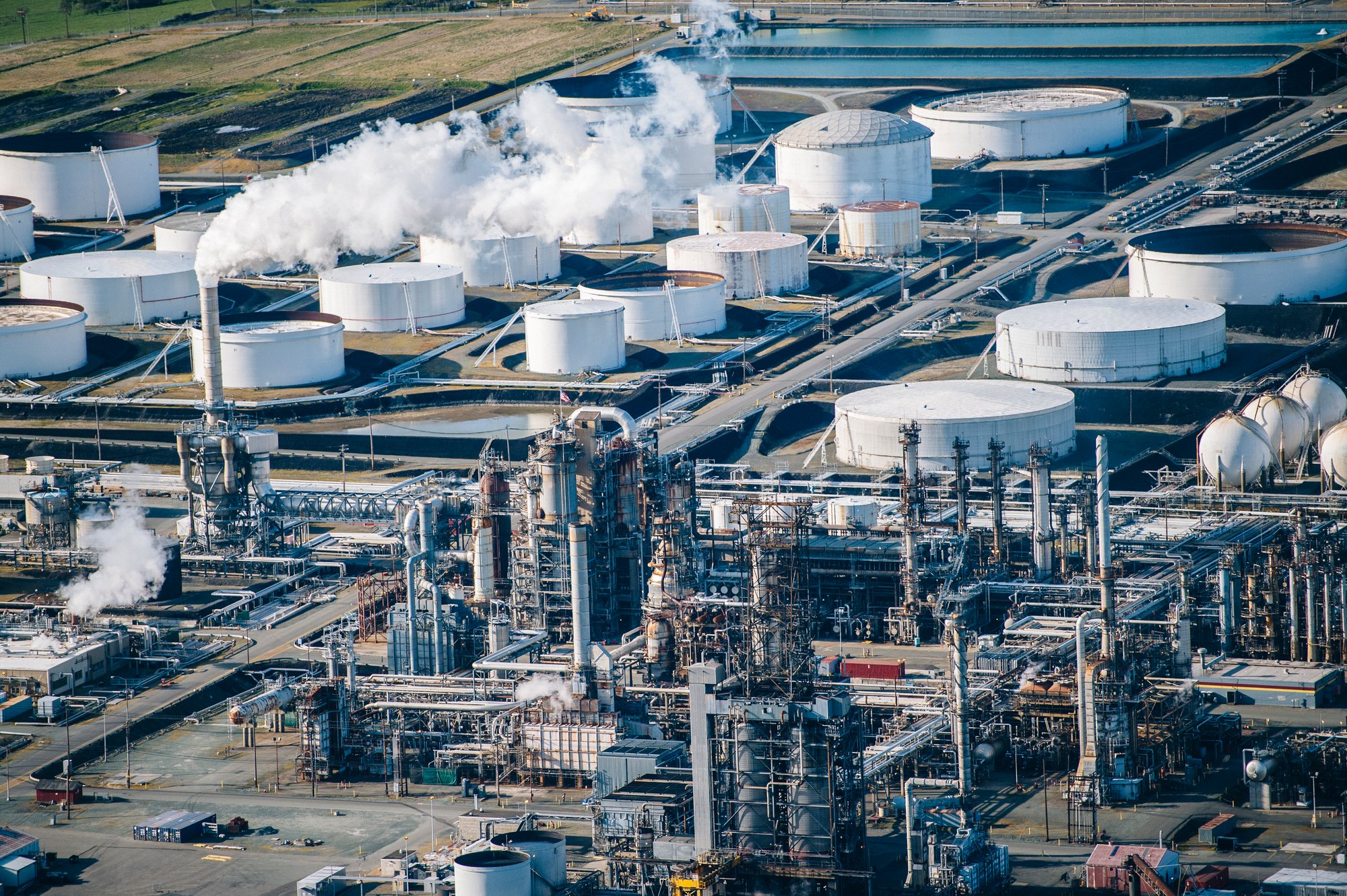 rows-of-white-oil-storage-tanks-and-smoke-stack-in-2024-06-11-18-45-38-utc